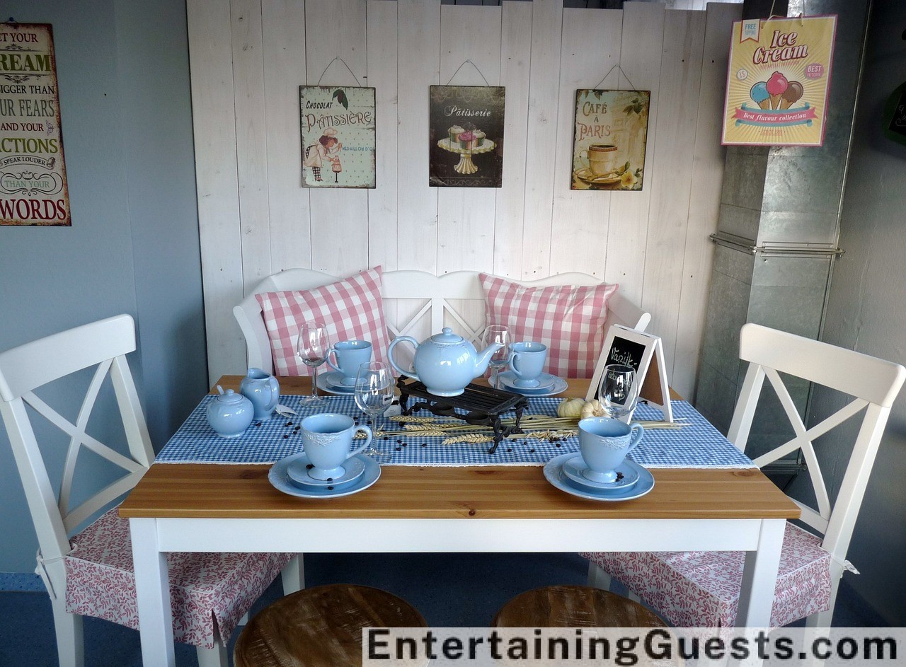 A cozy guest room with plush bedding, soft lighting, a stack of books, a warm throw blanket on an inviting chair, and a small tray with a tea set and fresh flowers