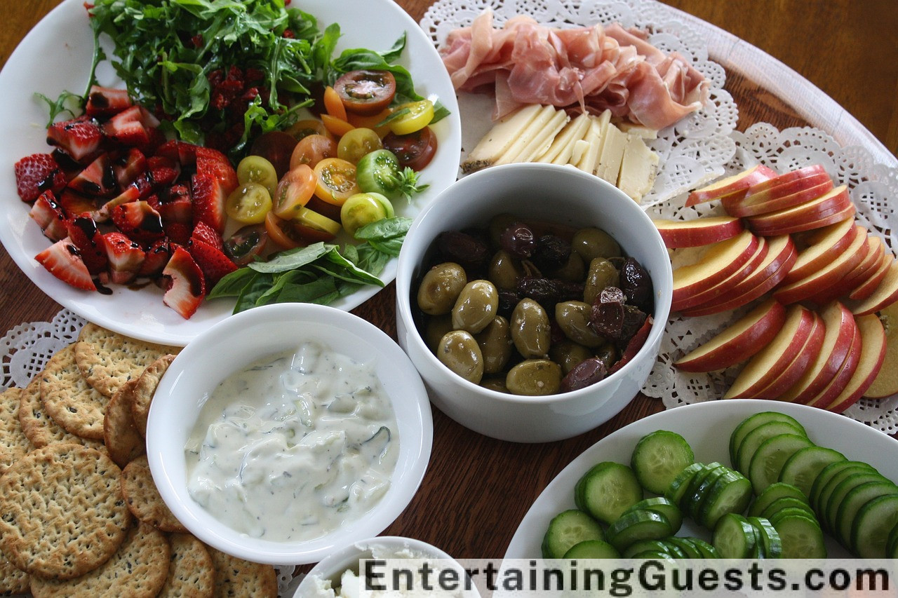 An image featuring a vibrant charcuterie board, with assorted cheeses, cured meats, fresh fruits, nuts, and crackers, surrounded by guests laughing and enjoying the food at a cozy, warmly-lit dinner party